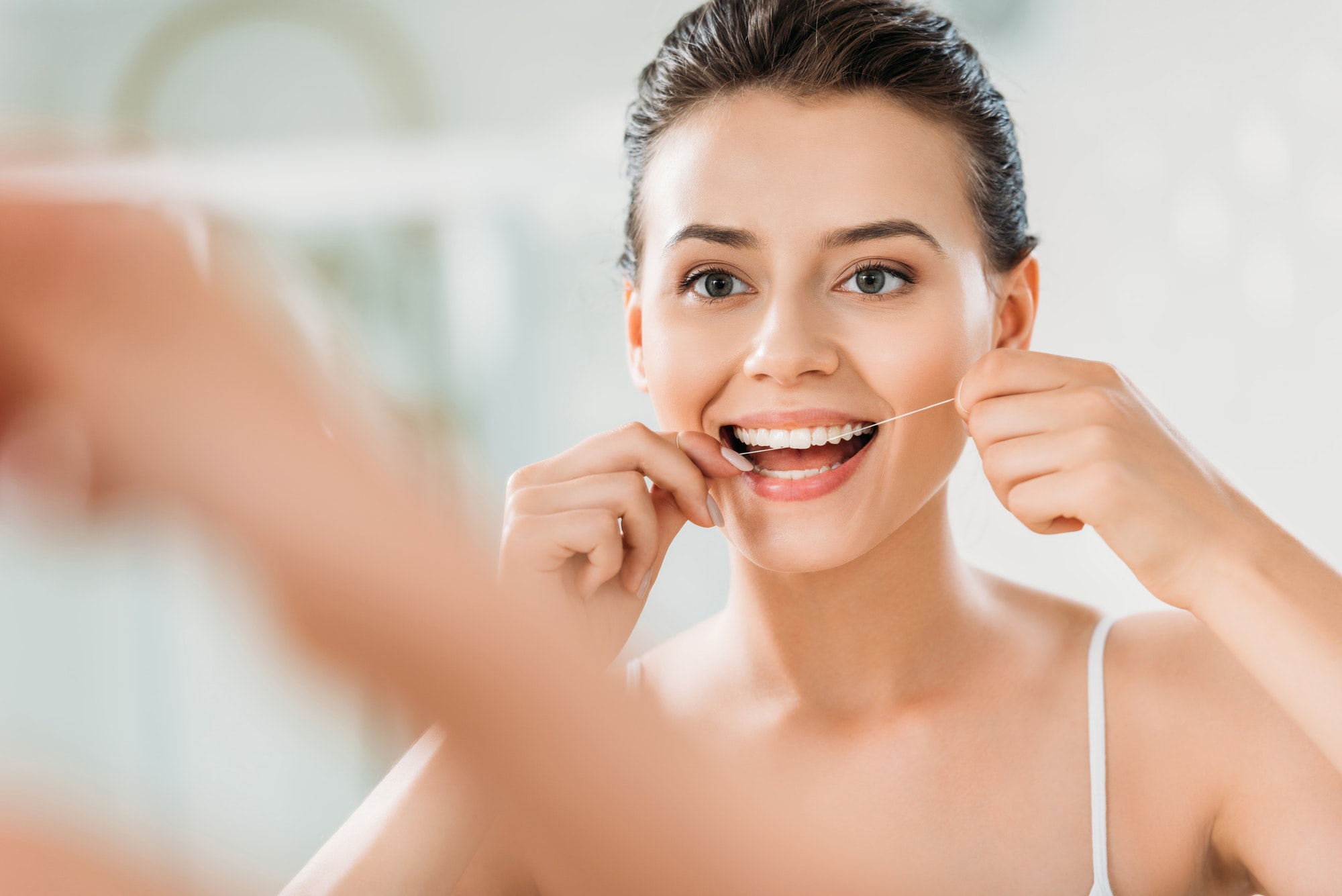 selective focus of beautiful smiling girl using dental floss in bathroom